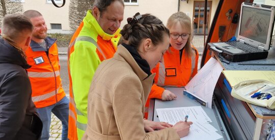 Eine Gruppe von Menschen steht an einem Messbus und unterschreibt ein Protokoll